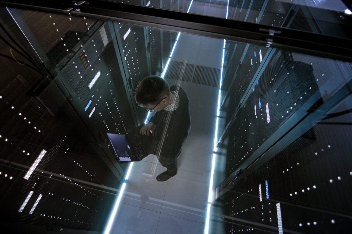 A person holding a laptop doing maintenance on a mainframe computer